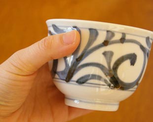砥部焼・梅山窯 からくさの湯呑(大)を手に持って